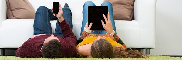 Des personnes allongées sur leur tapis en regardant leurs smartphone et tablette